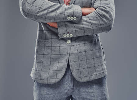 Man with crossed hands in grey checkered blazer and grey trousers on grey background.の写真素材