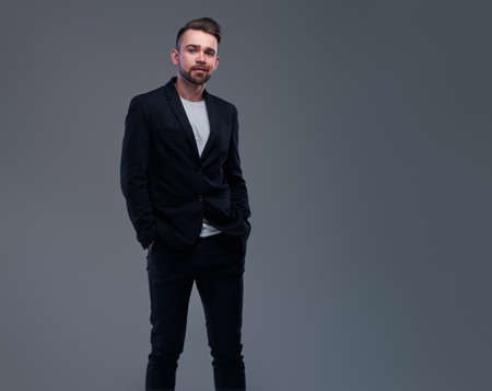 Studio shoot of trendy casual man in black suit and white t-shirt on grey background.