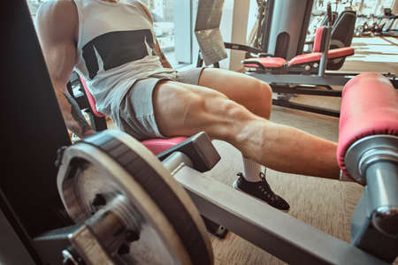 Strong muscular man is doing legs exercises on training apparatus.の写真素材