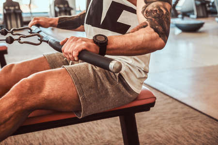 Young muscular man with tattoes is doing exercises on the rowing machine in the gym.の写真素材