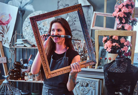 Pretty funny artist is posing with frame and brush in cozy art studio.