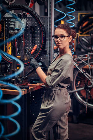 Diligent beautiful girl is repairing bicycle at busy workshop.の写真素材