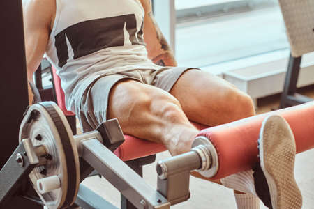 Strong muscular man is doing legs exercises on training apparatus.