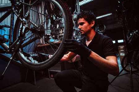 Handsome diligent master is fixing bicycles wheel at his workplace.の写真素材