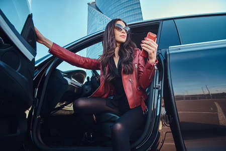 Beautiful smart women is posing in her new car while chatting on mobile phone. She is wearing red...