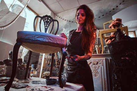 Young attractive artist is doing chair restouration in her own studio.の写真素材