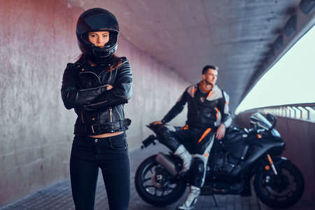 Couple of young bikers is relaxing in quiet tunnel with their motobike. Girl is wearing helmet. Man...
