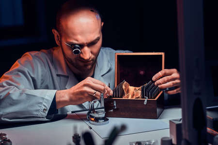 Focused man is working at his workshop with monocle and other tools repairing old watches.