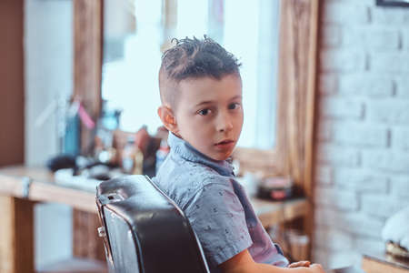 Small pretty boy is showing his new hairstyle while sitting at barbershop.の写真素材