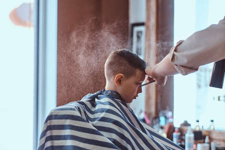Little charming boy is getting trendy haircut from mature hairdresser at fashionable hairdressing salon.の写真素材