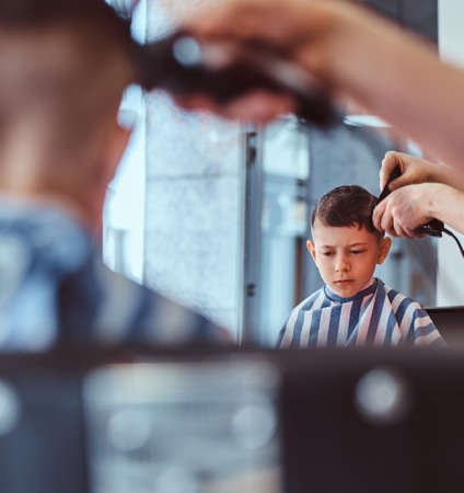 Little pretty school boy had his first trendy haircut at modern barbershop.の写真素材