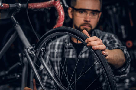 Handsome serious man in protective glasses is fixing bicycle at his own shop.の写真素材