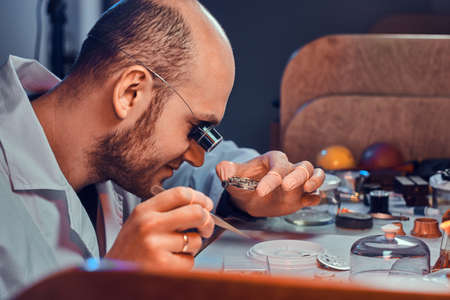 Mature clock master is fixing old watch for a customer at his busy repairing workshop.の写真素材