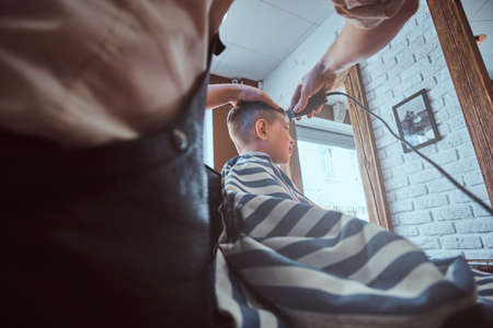 Small school boy is getting trendy haircut from expirienced barber at modern barbershop.の写真素材