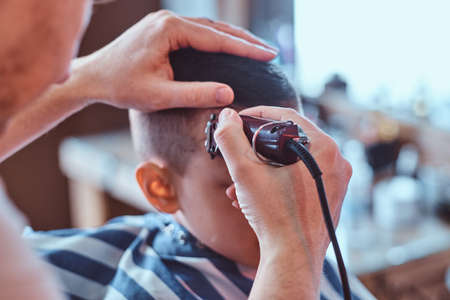 Funny little boy is getting trendy haircut from expirienced barber at fashionable hairdressing salon at firs time.の写真素材