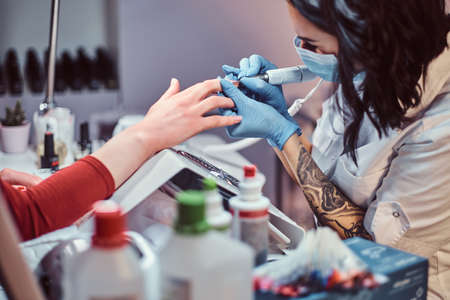 Hardware manicure in a beauty salon. Manicure procedure in progress - Beautician master using nail drill to trim and remove cuticlesの写真素材
