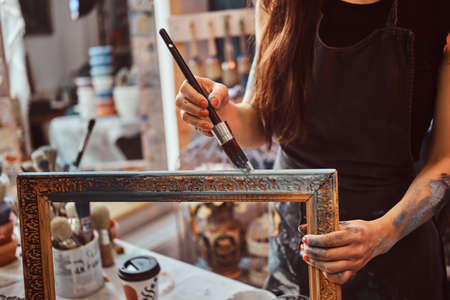 Young talented painter is restourating old frame in her own workshop.