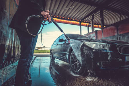 Smart trendy man in jeans is washing his own car at car washing station.の写真素材