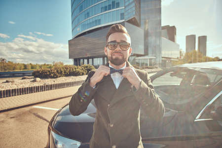 Smiiling happy man in coat is standing near his new car at the parking.の写真素材