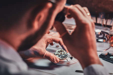 Mature clock master is fixing old watch for a customer at his busy repairing workshop.の写真素材