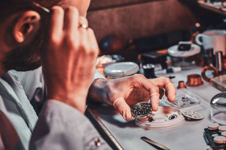Mature clock master is fixing old watch for a customer at his busy repairing workshop.の写真素材