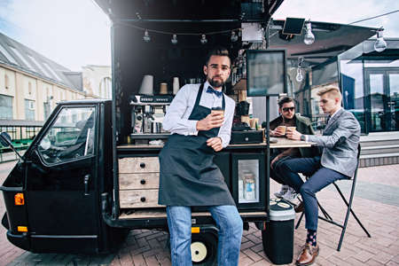 Handsome groomed barista  have a coffee break near his small coffee shop.の写真素材