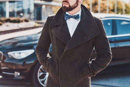 Smart groomed man in coat is standing near his new car.の写真素材