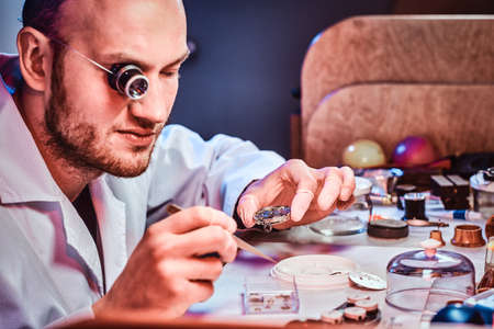 Mature clockmaster is fixing old watch for a customer at his busy repairing workshop.の写真素材