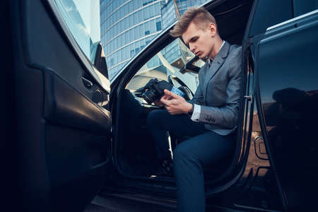 Young attractive buisnisman is looking to his mobile phone while sitting in the car.