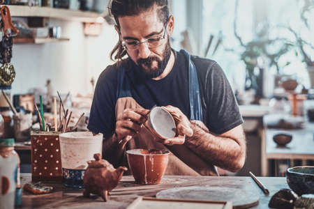 Diligent man is putting colourful clay to his new handmade pot.の写真素材