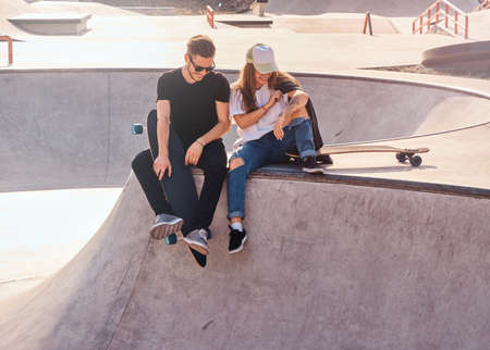 Smiling happy couple of students are sitting at skatepark with their longboards.の写真素材