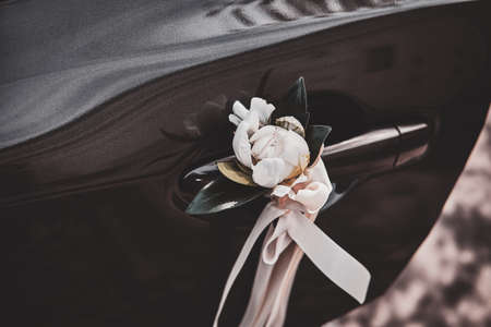 Closeup photoshoot of decorater cars door with white roses and silk bow.