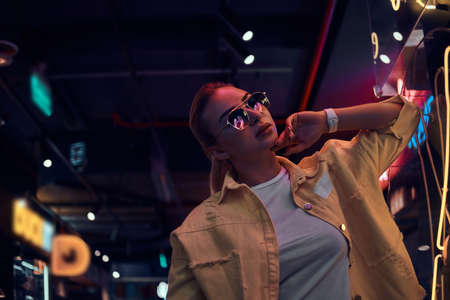 Portrait of pensive trendy woman in neon lights with darkness around.の写真素材