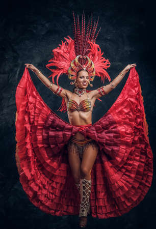 Talented joyful can can dancer in red feather costume is posing at small dark studio.の写真素材