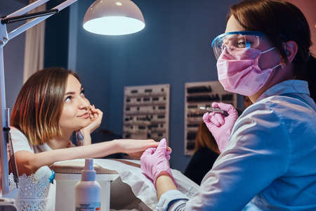 Pretty dreamy woman with tattoo got nail care from young dilligent manicurist.の写真素材