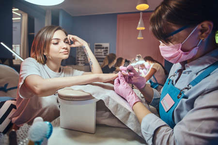Attractive young woman with tattoo is getting nail care from expirienced manicurist.