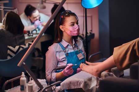 Process of pedicure at busy nail studio. Customer is getting good service from beautiful diligent...