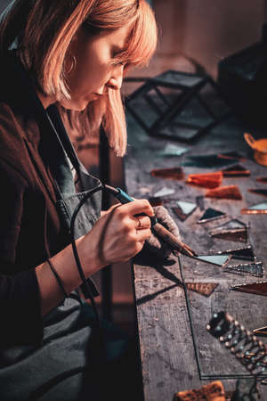 Expirienced designer is working with soldering iron at her own cozy workshop.の写真素材