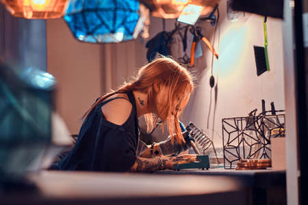 Dilegent pensive woman is working on her own lamp project at cozy workshop.の写真素材