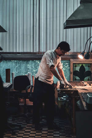 Focused glazier is working on old broken stained glass restoration at his own workplace.の写真素材