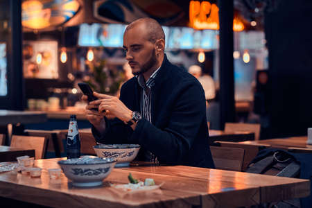 Serious sucessful businessman is chatting by mobile phone while sitting at restaurant.の写真素材