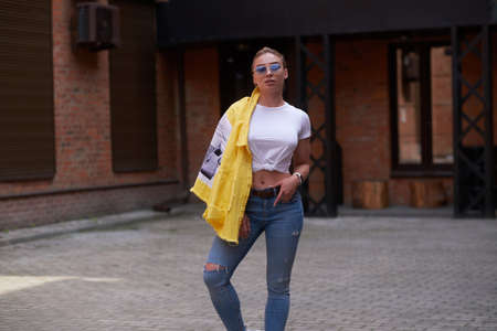 Cheeky trendy woman in sunglasses is posing for photographer at random city yard.