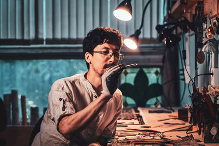 Dilligent focused master is looking for right  peace of glass for his project. workshop at background.の写真素材