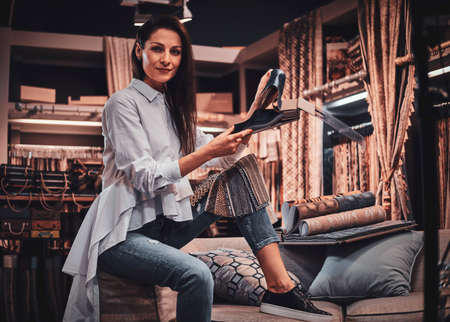 Smiling happy womas is sitting on the sofa at her cozy textile workshop. She keeps drawings in her hands.の写真素材