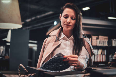 Elegant cheerful woman is sitting at her workplace while choosing patterns for her new project.