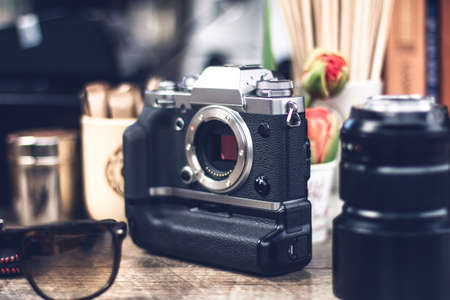 Body of digital camera on the table and another things around, like objective, sunglasses, cups and...