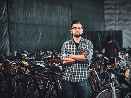 Pensive man in protective glasses and checkered shirt is posing at his own warehouse full of bicycles.の写真素材