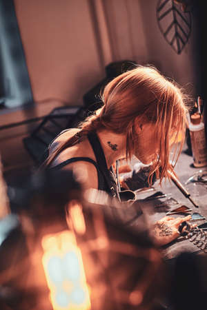 Dilegent pensive woman is working on her own lamp project at cozy workshop.の写真素材