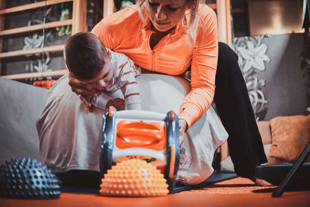 Nice expirienced pediatrician is doing special ortophedic exercises for little cute toddler with toys at her cabinet.の写真素材