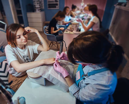 Process of manicure at beuaty salon with two attractive happy womens.